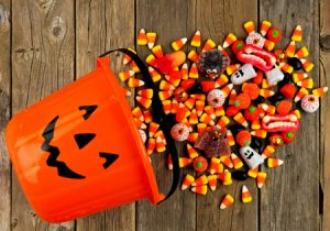 Halloween Jack o Lantern pail with spilling candy, above view on a rustic wood background